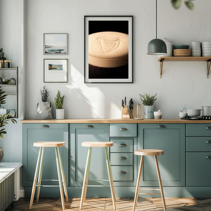 A vertical macro photograph of the thick, creamy foam head on a pint of Guinness. The iconic Guinness harp is embossed into the center of the velvety bubbles. The image features warm cream tones against a dark, shadowy background.