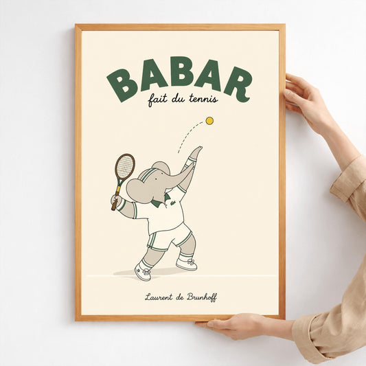 A vertical minimalist art print of Babar the Elephant playing tennis. Babar is shown in profile against a solid light cream background, wearing a white tennis outfit with green accents and a striped headband. He is holding a tennis racket and has just tossed a yellow tennis ball into the air to serve. At the top, bold dark green text reads "BABAR" with a gold crown above it and "fait du tennis" in script below. The artist's name is centered at the bottom.