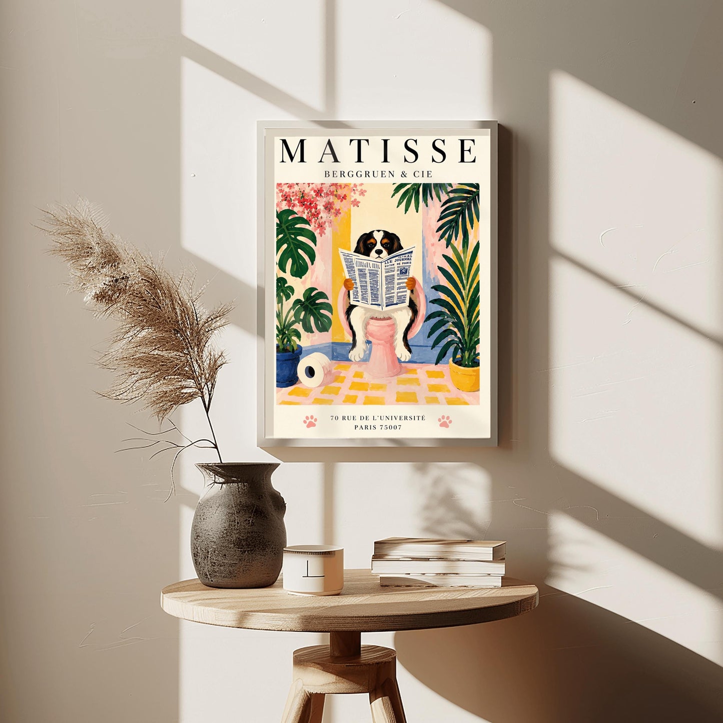 A vertical vintage-style exhibition poster on a cream background titled "MATISSE BERGGRUEN & CIE" in bold black font. The main gouache-style illustration depicts a tricolor black, white, and tan Cavalier King Charles Spaniel sitting on a pink toilet. The dog is holding and reading a blue-and-white French newspaper titled "LE JOURNAL". The bathroom scene includes a roll of toilet paper on a yellow checkered floor, potted monstera and palm plants