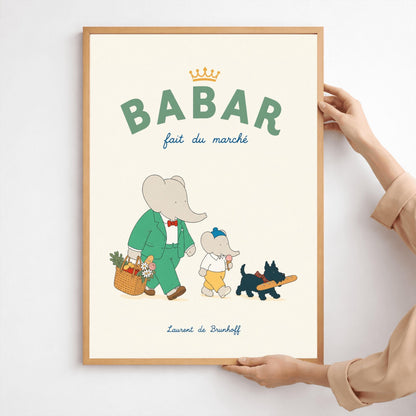 A vertical storybook-style art print of Babar the Elephant walking home from a market against a cream background. Babar is in a green suit and red bow tie, carrying a basket of fruit and flowers. Beside him is a smaller elephant eating an ice cream cone and a small black dog in a plaid collar carrying a baguette. The top text reads "BABAR fait du marché" with a gold crown.