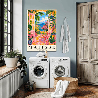 A vertical maximalist art print styled as a Henri Matisse exhibition poster. The scene features a vibrant balcony with pink-framed glass doors open to a view of the blue Mediterranean sea and a coastal town. The balcony has pink and yellow checkered tiles, a yellow round table with a pink chair, and is filled with tropical plants and pink flowers in blue and white vases. A sailboat is visible on the water under a bright blue sky with white clouds.