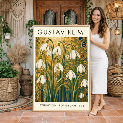 A vertical retro exhibition poster for Gustav Klimt featuring a wide cream-colored border. The central image shows an intricate Art Nouveau illustration of a cluster of delicate white snowdrop flowers with long green leaves reaching upward. The background is an opulent, decorative tapestry of metallic gold patterns, featuring detailed concentric circles, swirling spirals, and tiny mosaic tiles accented with hints of blue and teal.