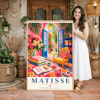 A vertical maximalist art print styled as a Henri Matisse exhibition poster. The scene shows a vibrant interior reading room with hot pink walls and cobalt blue French doors open to a sunlit garden. A yellow cane chair sits next to a bookshelf. In the foreground, a table covered in a pink floral cloth holds a stack of art books, an open book, and a blue coffee mug. Large monstera leaves and various flowers frame the room. Bold black and red text at the bottom reads "MATISSE PAPIERS DÉCOUPÉS"