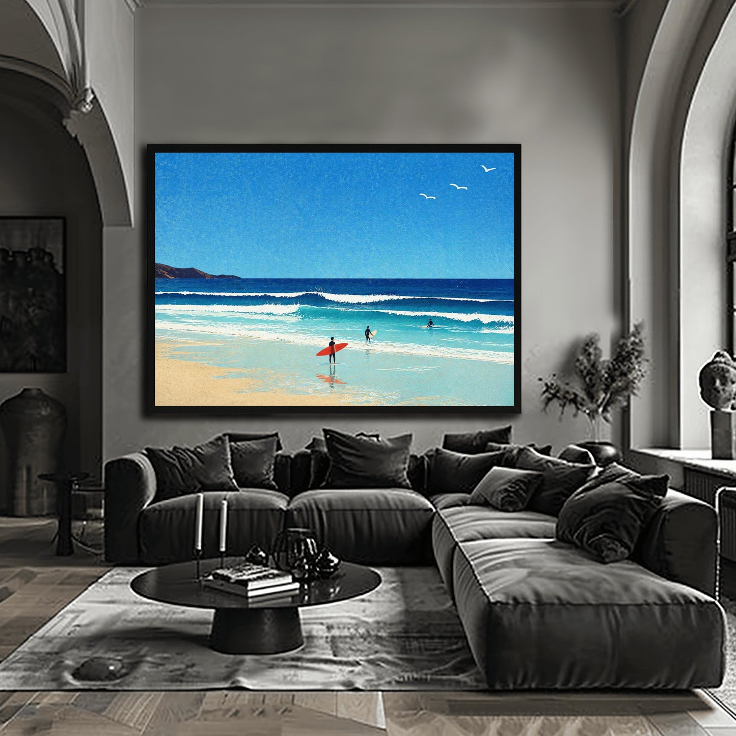 A horizontal minimalist art print of a bright beach day. A vast blue sky with three small white birds in flight sits above a turquoise ocean with gentle white waves. In the foreground, a sandy beach meets the water. A lone surfer in a black wetsuit holds a bright red surfboard on the shore, while two other surfers are further out in the water. A dark cliff is visible on the far left horizon. The style is clean and graphic with a subtle paper texture.