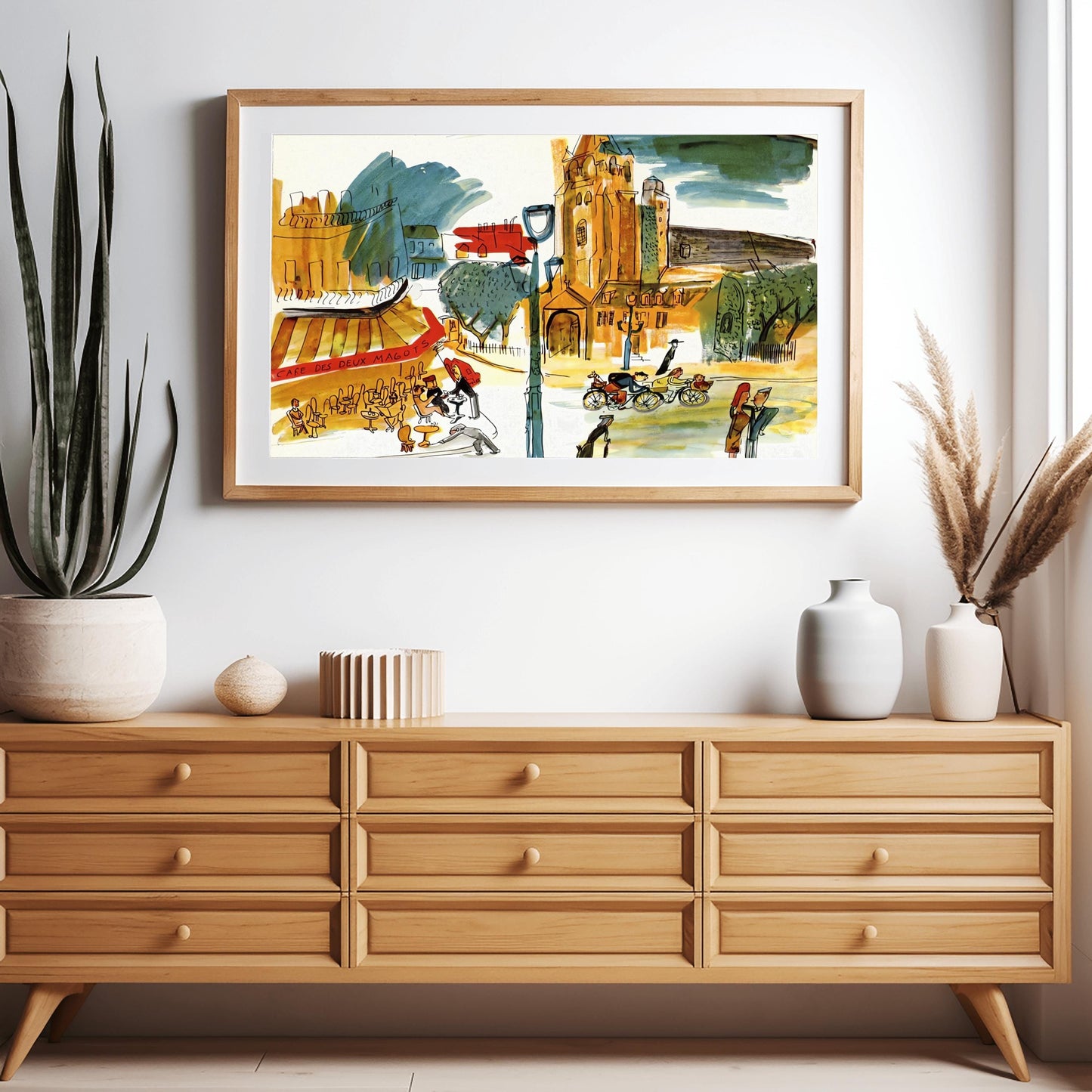A horizontal whimsical watercolor illustration of a busy Paris street corner. To the left, patrons sit at small tables under a red and yellow striped awning labeled "CAFE DES DEUX MAGOTS." In the center, a large, warm-toned stone church with a tall tower rises against a sky with dark blue and green clouds. Various figures populate the street, including people on bicycles, a waiter, and pedestrians. The artwork uses loose black outlines and vibrant, sketchy color washes in orange,yellow,and green