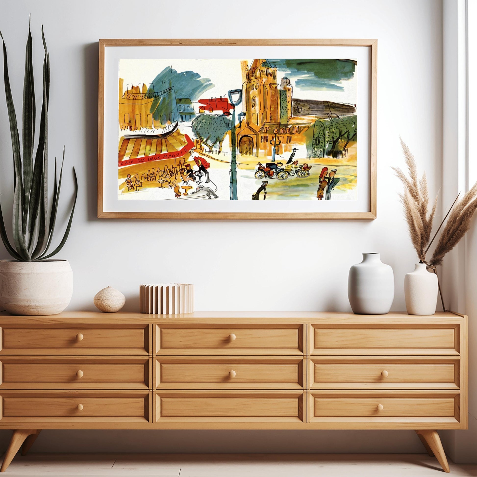 A horizontal whimsical watercolor illustration of a busy Paris street corner. To the left, patrons sit at small tables under a red and yellow striped awning labeled "CAFE DES DEUX MAGOTS." In the center, a large, warm-toned stone church with a tall tower rises against a sky with dark blue and green clouds. Various figures populate the street, including people on bicycles, a waiter, and pedestrians. The artwork uses loose black outlines and vibrant, sketchy color washes in orange,yellow,and green