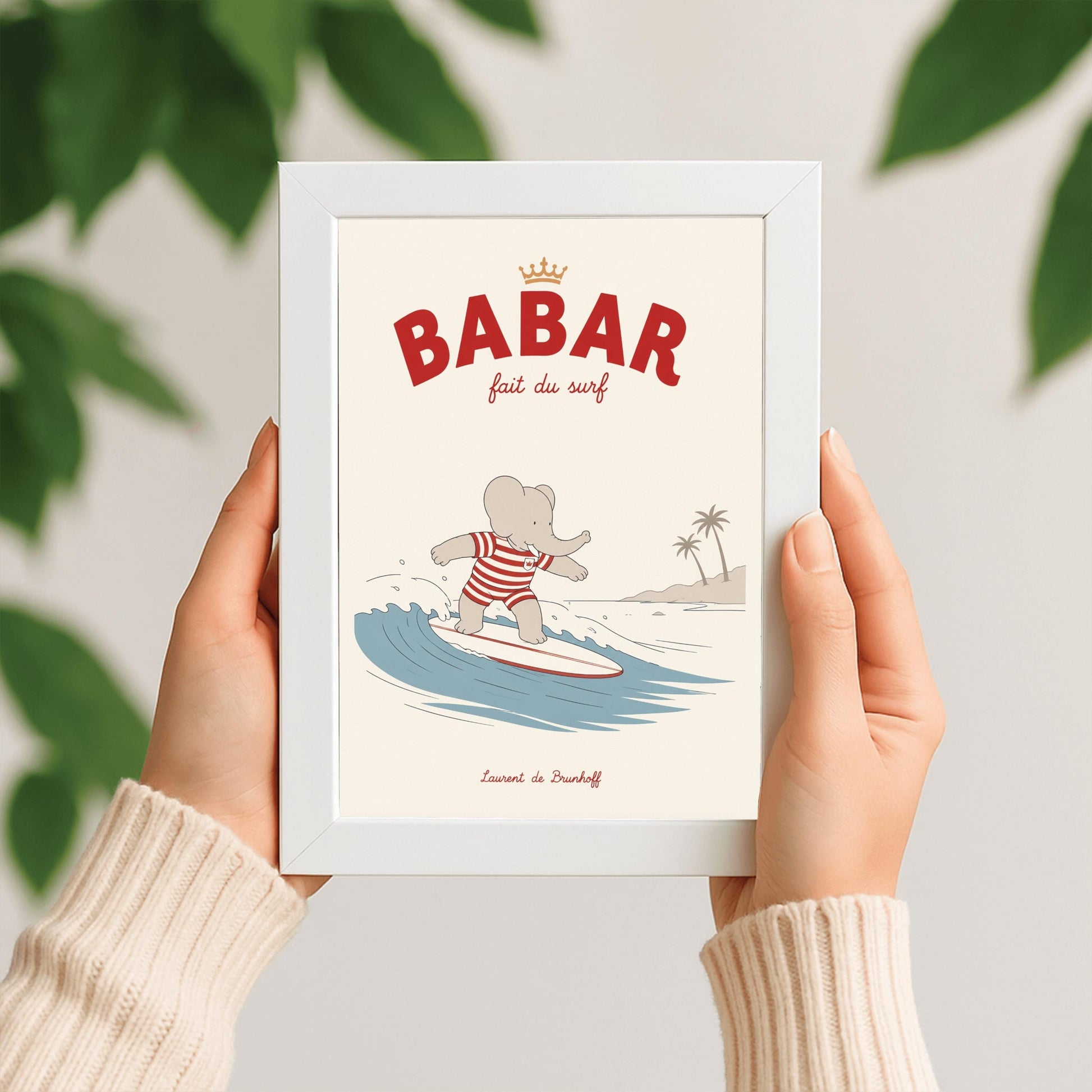 A vertical storybook-style art print of Babar the Elephant surfing. Babar is wearing a red and white striped swimsuit and standing on a white surfboard with a red stripe. He is riding a blue wave with a white crest. In the background, there is a tan beach with two palm trees under a cream sky. The top reads "BABAR fait du surf" with a small gold crown.