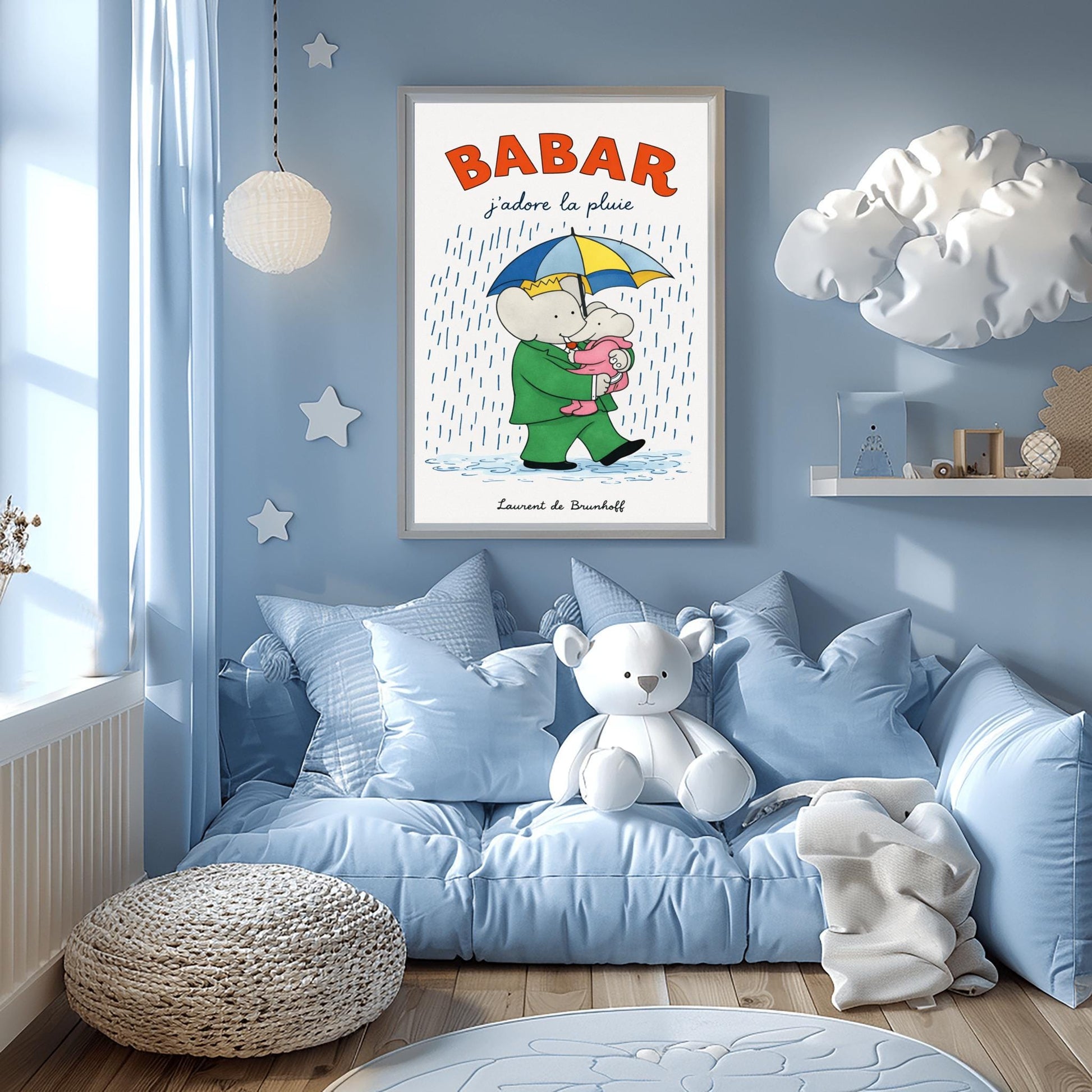 A vertical children's illustration poster titled "BABAR: j'adore la pluie" in orange and blue. King Babar, in a green suit and crown, is walking through the rain while holding a blue and yellow striped umbrella. He is carrying a small elephant wearing a pink rainsuit. They are walking through light blue puddles on a white background. The name "Laurent de Brunhoff" is at the bottom.